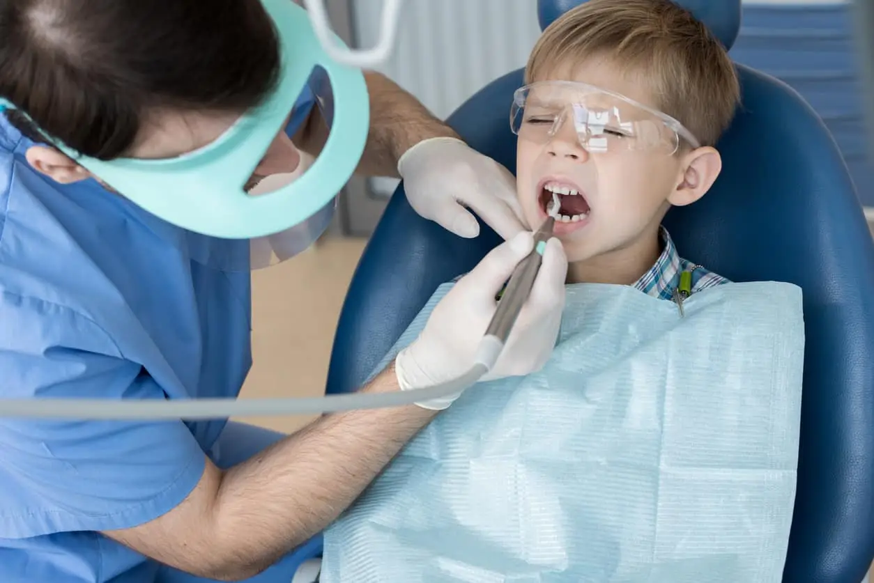 Young boy in a dentist chair wincing in pain from a toothache